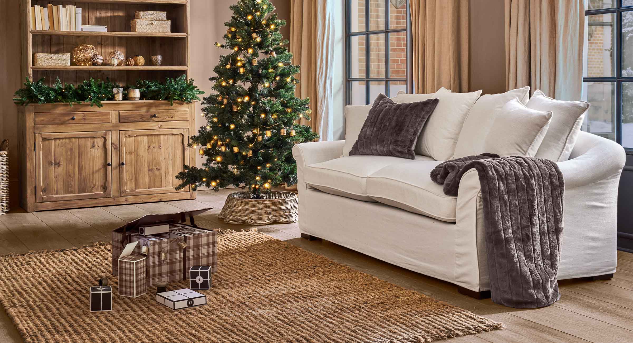 Soggiorno accogliente con divano bianco, cuscini marroni e albero di Natale illuminato