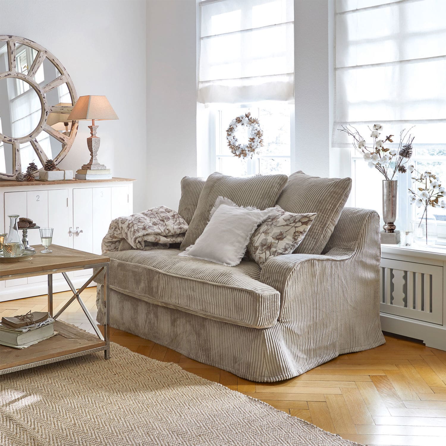 Divano Monaco Divano beige in velluto a coste in soggiorno luminoso con decorazioni naturali e tappeto in juta