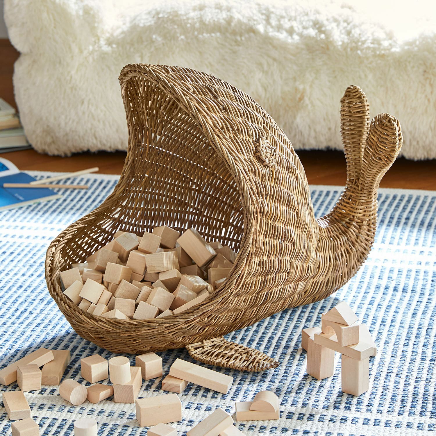 Cesto Cheruboo Cesto a forma di balena in vimini naturale con blocchi di legno su tappeto blu a motivi