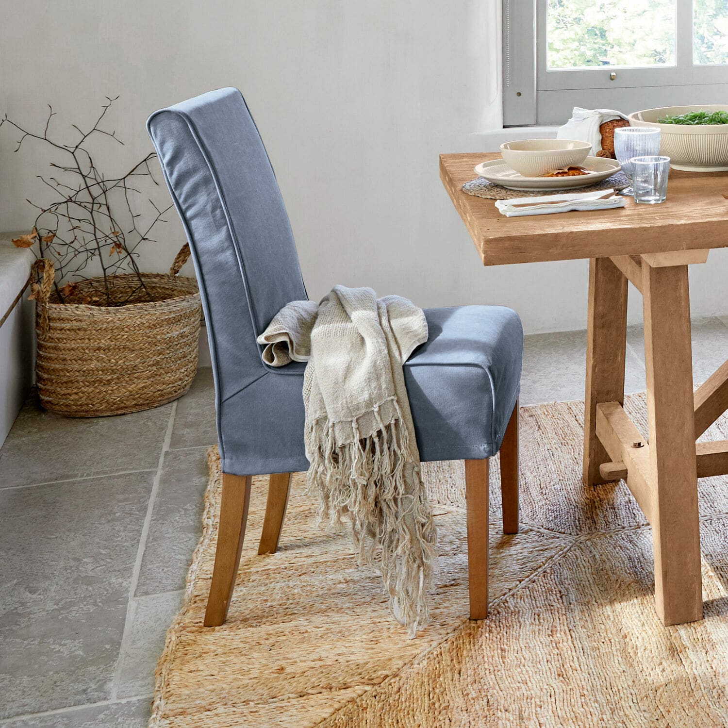 Sedia con coprisedia Mankato Sedia imbottita blu con gambe in legno e coperta beige accanto a tavolo in legno chiaro