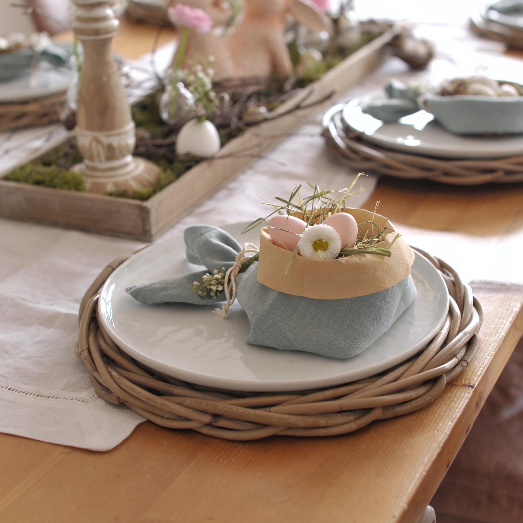 Decorazione da tavola con piatto bianco su sottopiatto in vimini e tovagliolo con uova e fiori