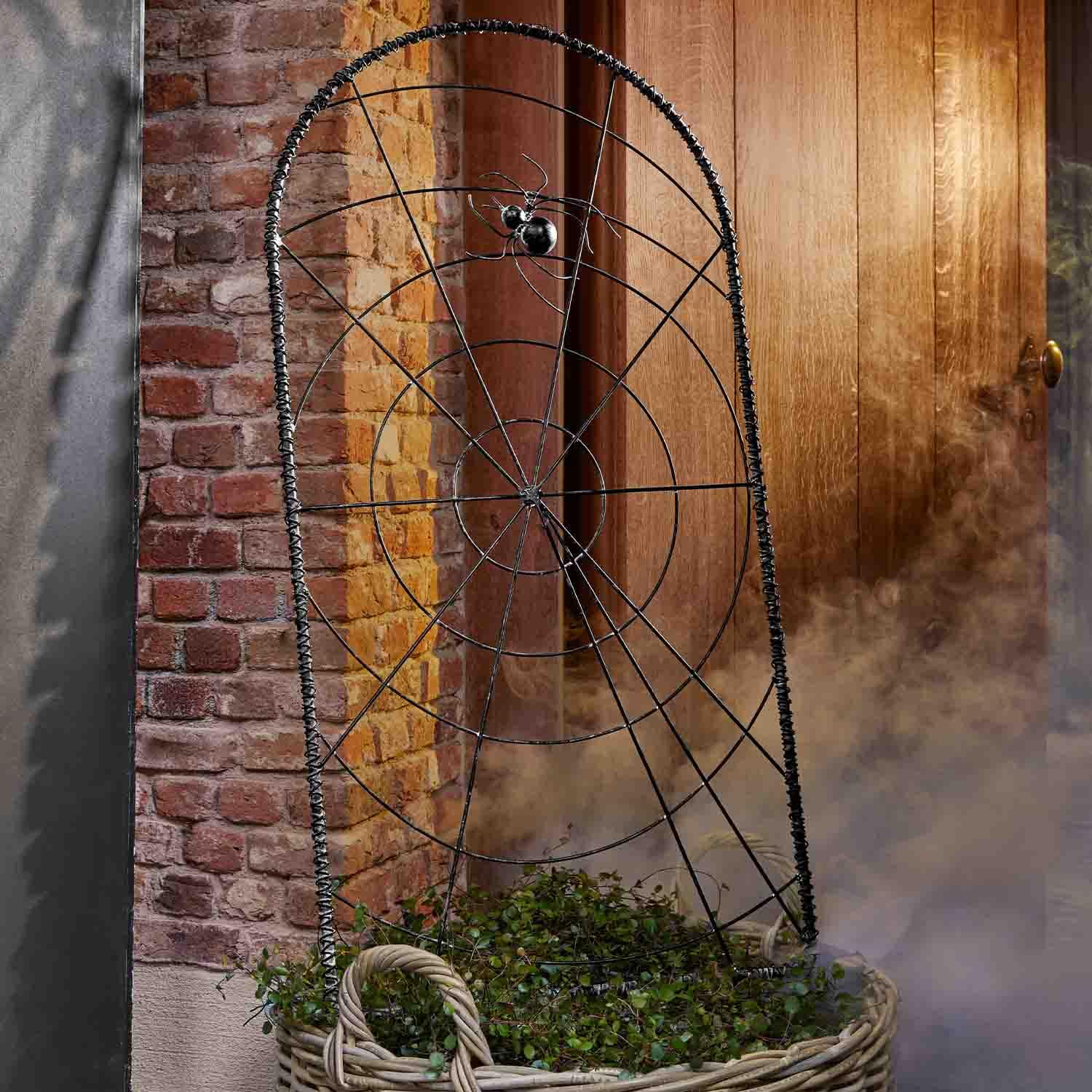Decorazione in metallo nero a forma di ragnatela con ragno davanti a muro di mattoni e porta in legno