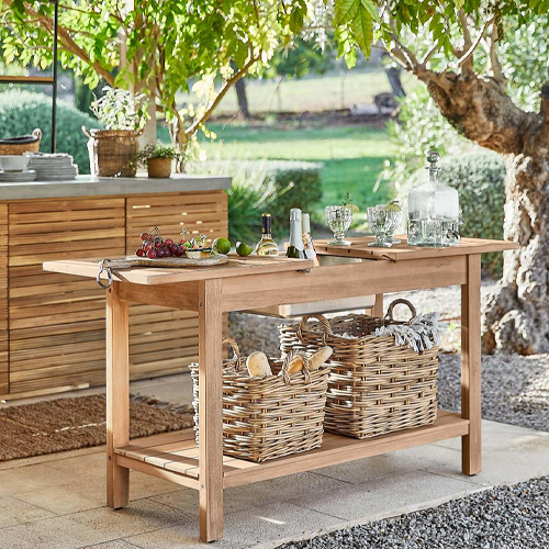 Tavolo da giardino in legno naturale con cesti di vimini e accessori per servire su terrazza soleggiata