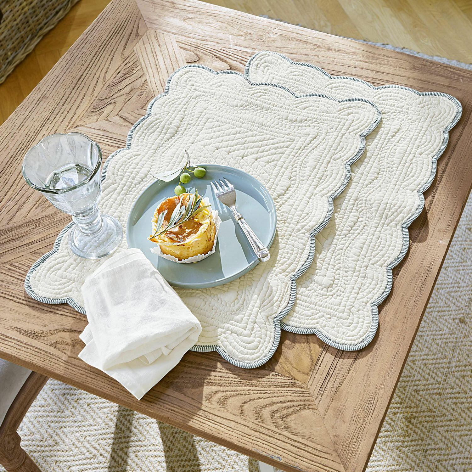 Coppia di tovagliette Fontienne Tovagliette trapuntate in cotone beige con bordo blu su tavolo in legno con dessert e bicchiere