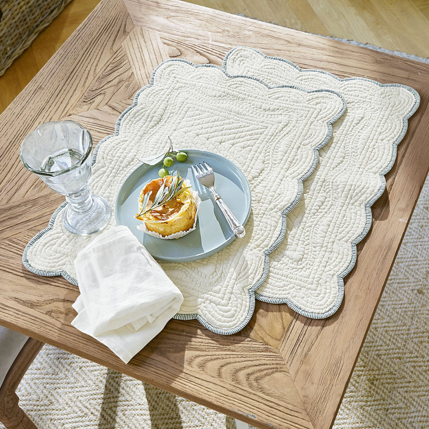Coppia di tovagliette Fontienne Tovagliette trapuntate in cotone beige con bordo blu su tavolo in legno con dessert e bicchiere