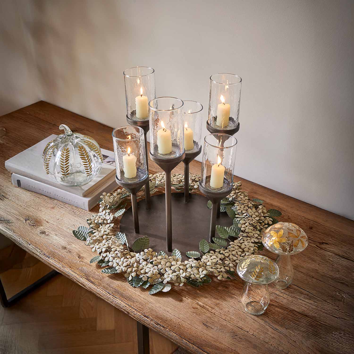 Portacandele in metallo con sei copri-candele in vetro e candele bianche su tavolo in legno con decorazioni