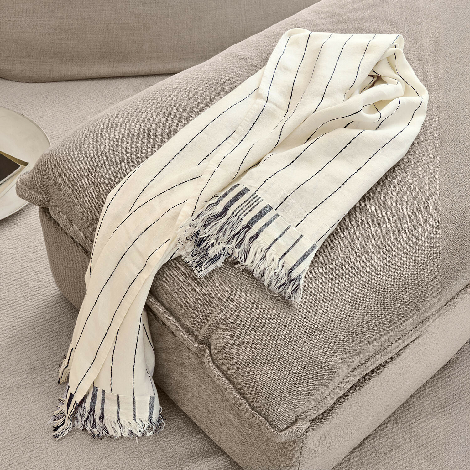 Coperta beige in cotone con righe nere e frange su poltrona grigia, decorazione accogliente per interni