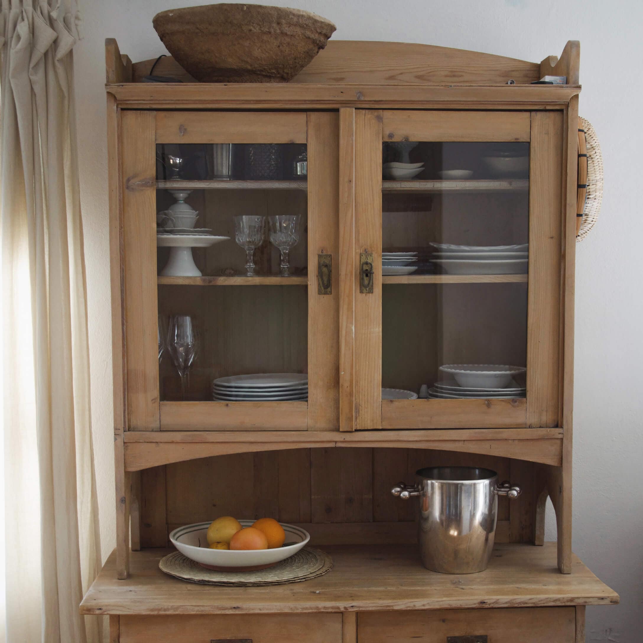 Credenza in legno con ante in vetro, stoviglie bianche e secchiello in metallo sul piano