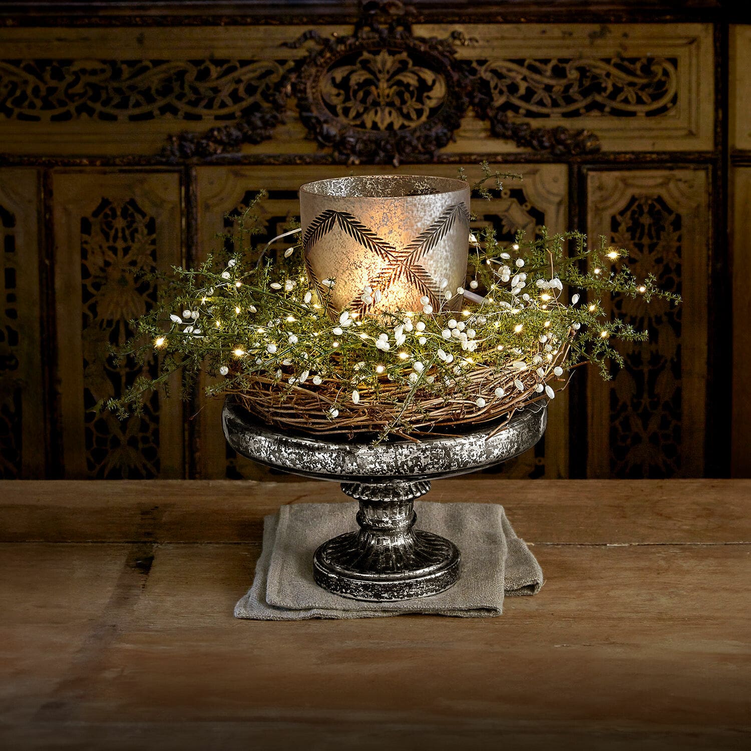 Alzata Incantesse Portacandele decorativo in metallo argentato con corona di vimini e luci LED su tavolo in legno