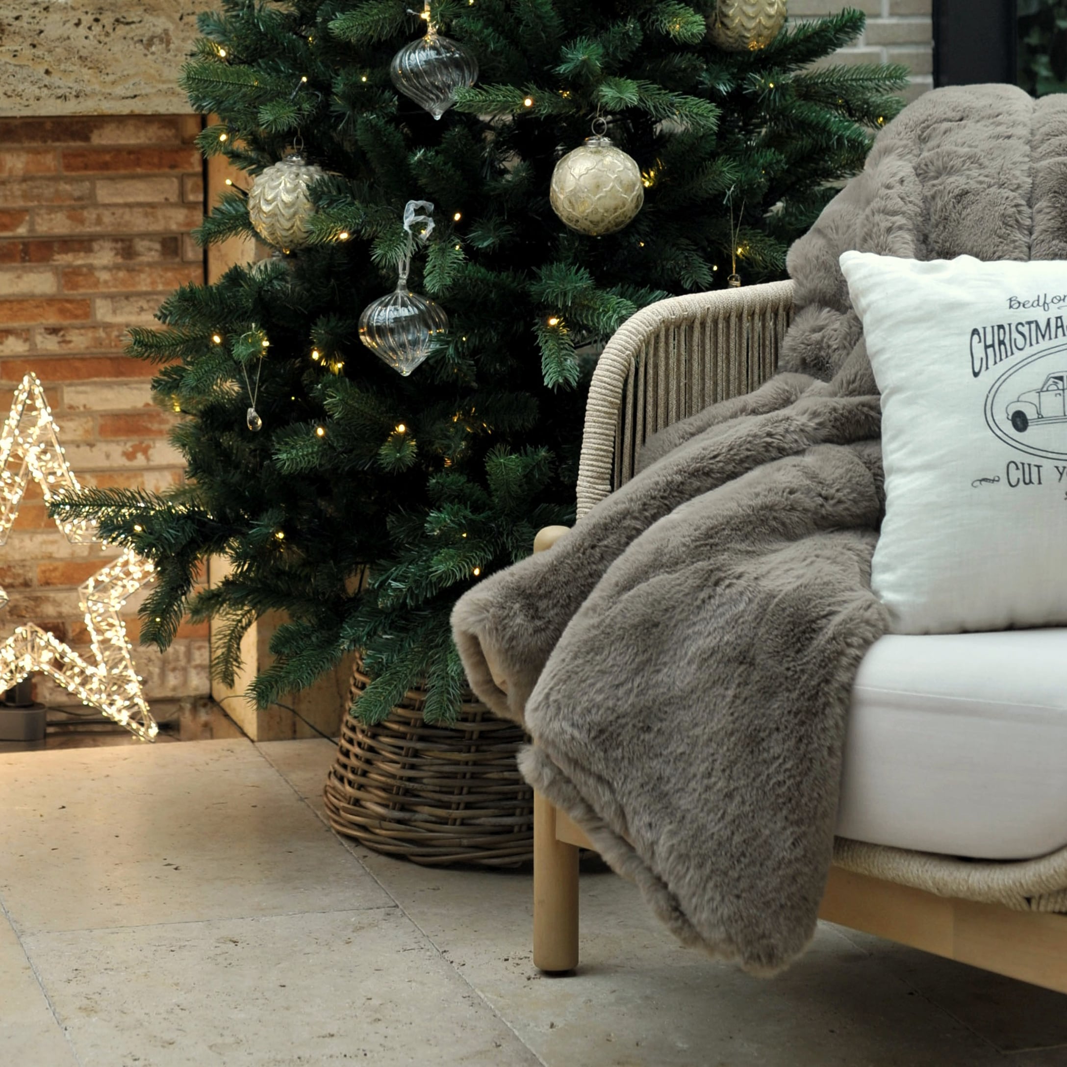 Coperta grigia in pelliccia sintetica su poltrona accanto ad albero di Natale decorato e stella luminosa