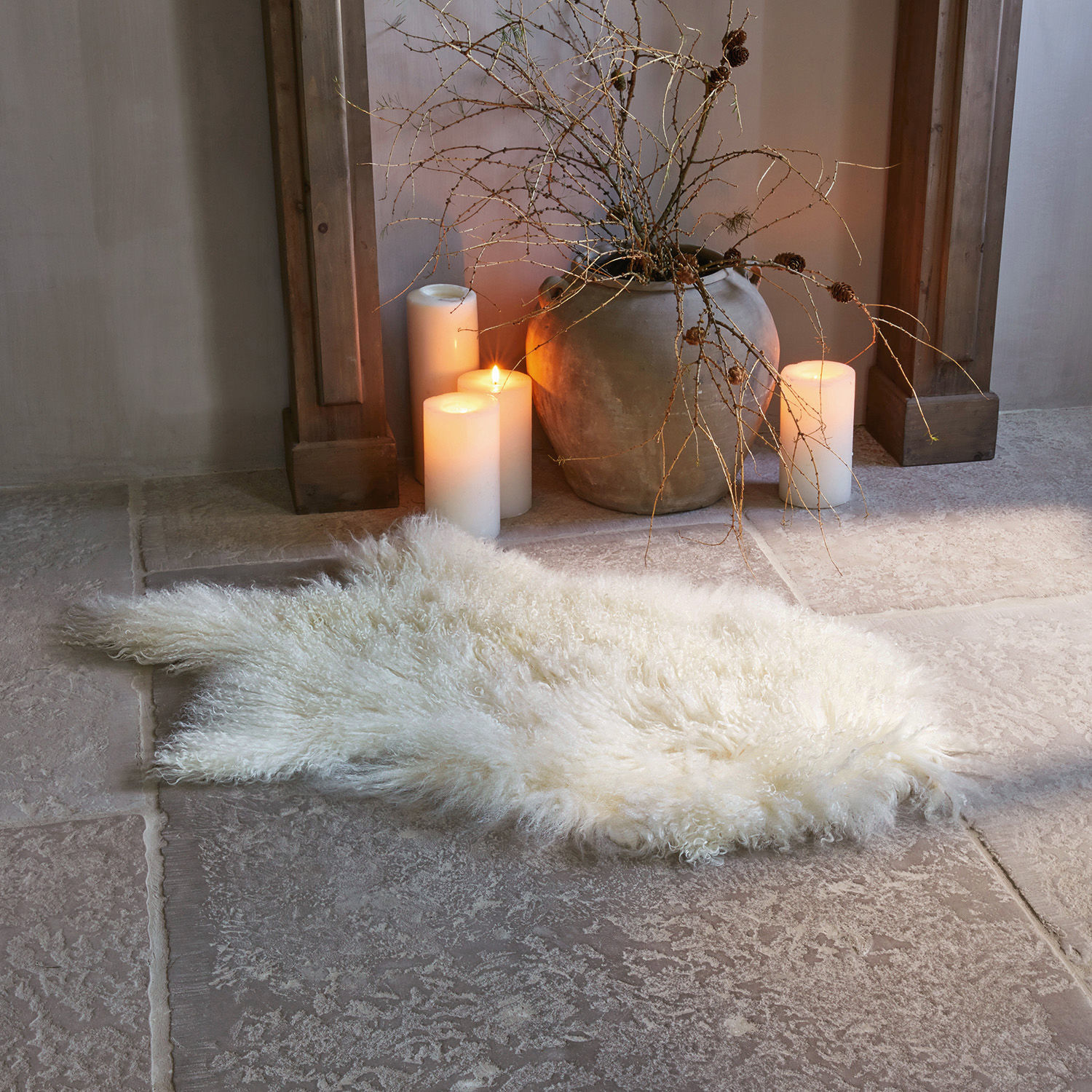 Vello di agnello Gad Tappeto bianco morbido in pelliccia su pavimento in pietra accanto a candele e vaso in terracotta