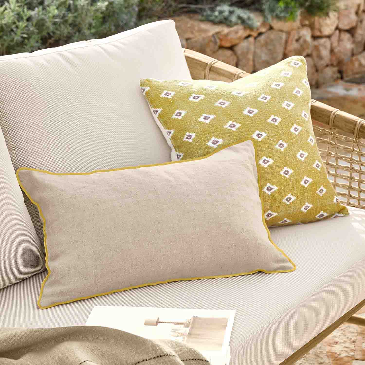 Cuscino beige con bordo giallo e cuscino giallo con motivo bianco su divano in rattan