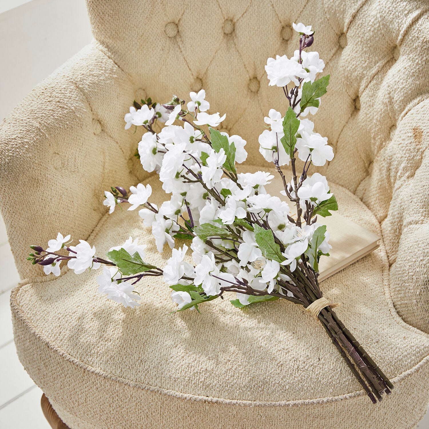 Set di 6 fiori decorativi Bellévaut Mazetto di fiori bianchi artificiali con foglie verdi su poltrona beige testurizzata