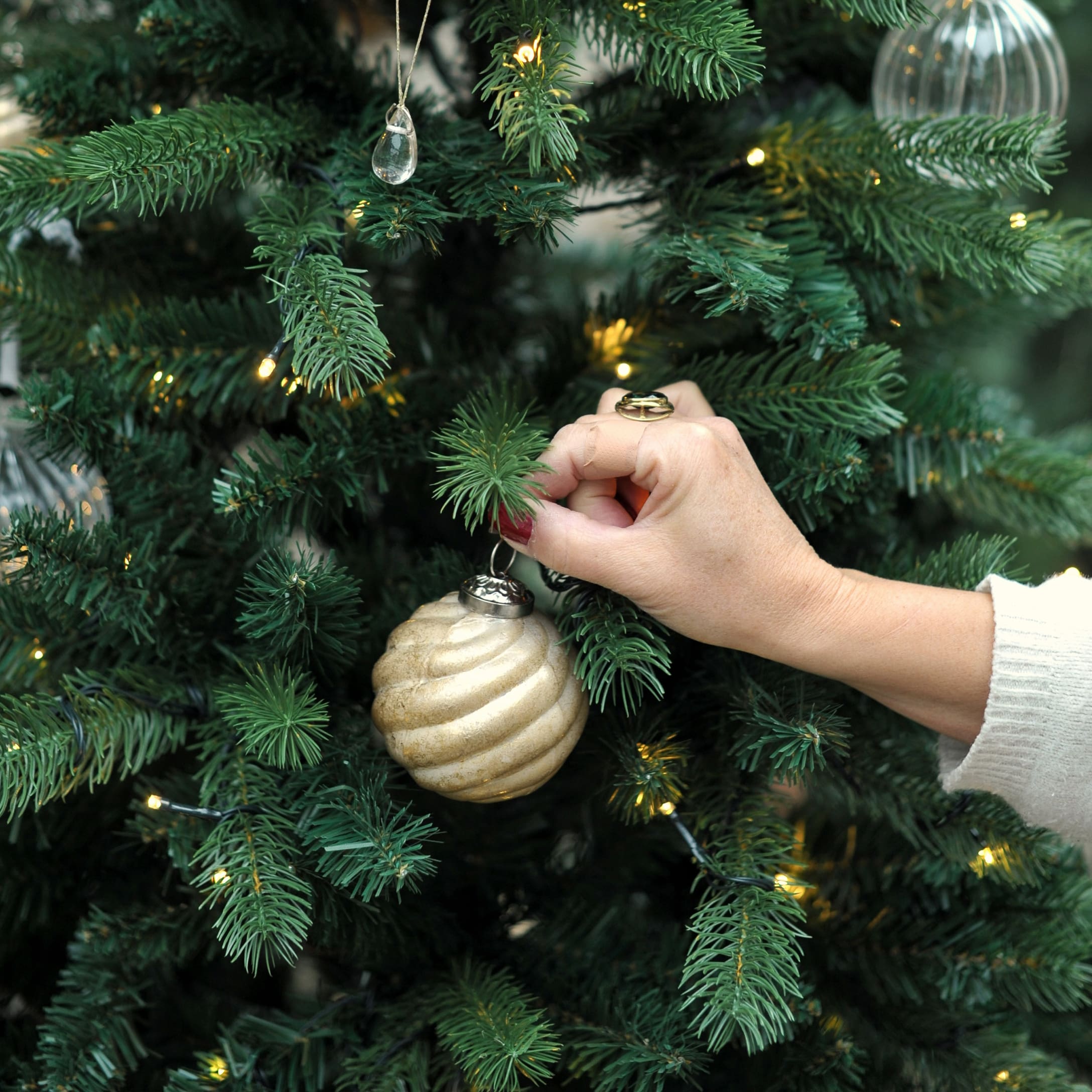 Mano che decora albero di Natale verde con pallina dorata a spirale e luci LED in veranda