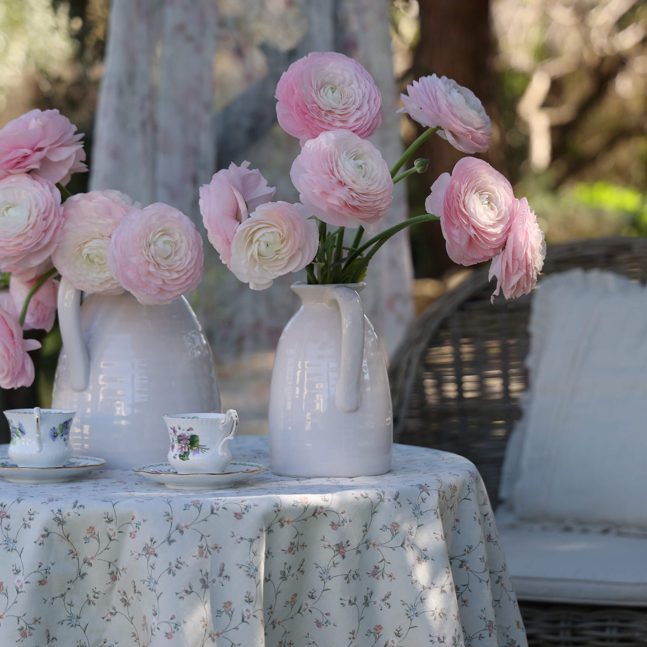 Brocche in ceramica bianca con fiori rosa su tavolo con tovaglia floreale e tazze da tè decorative