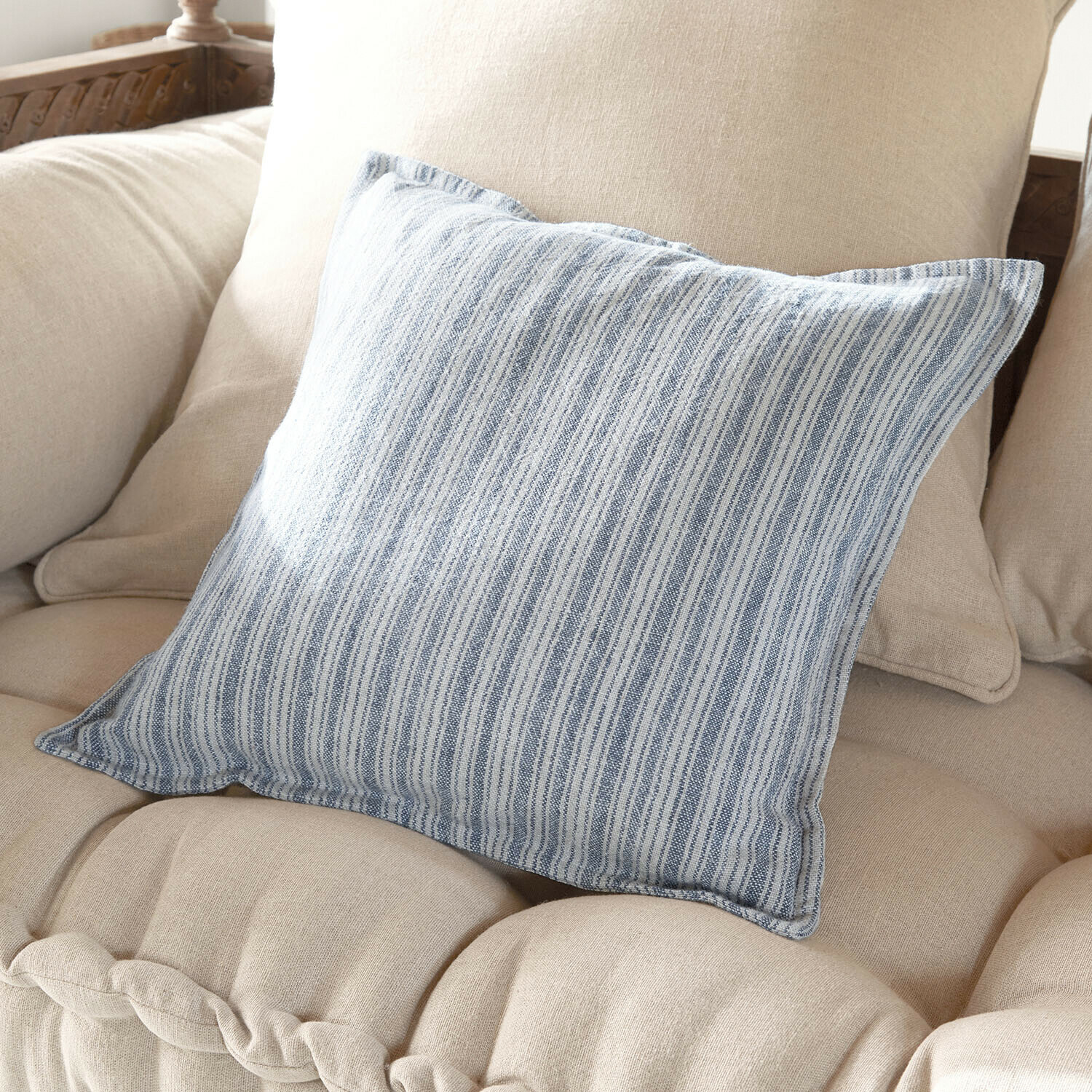 Cuscino decorativo in cotone a righe blu e bianco su divano beige, accessorio elegante per interni