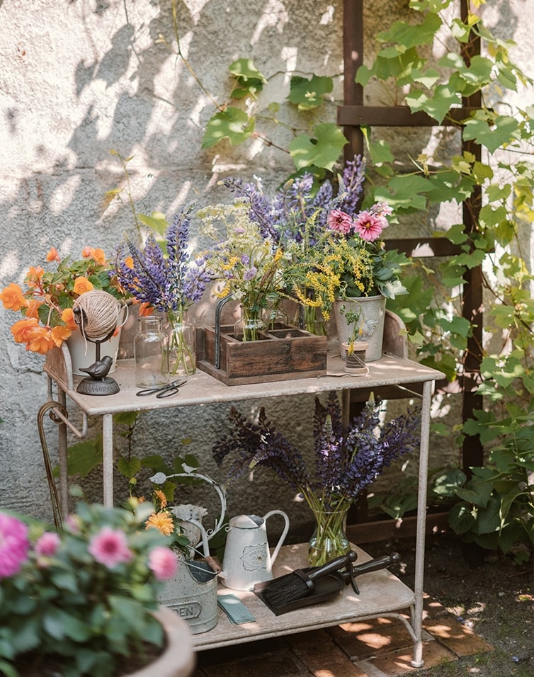 Tavolo da giardino in metallo con fiori e attrezzi da giardino in un angolo soleggiato e ombreggiato