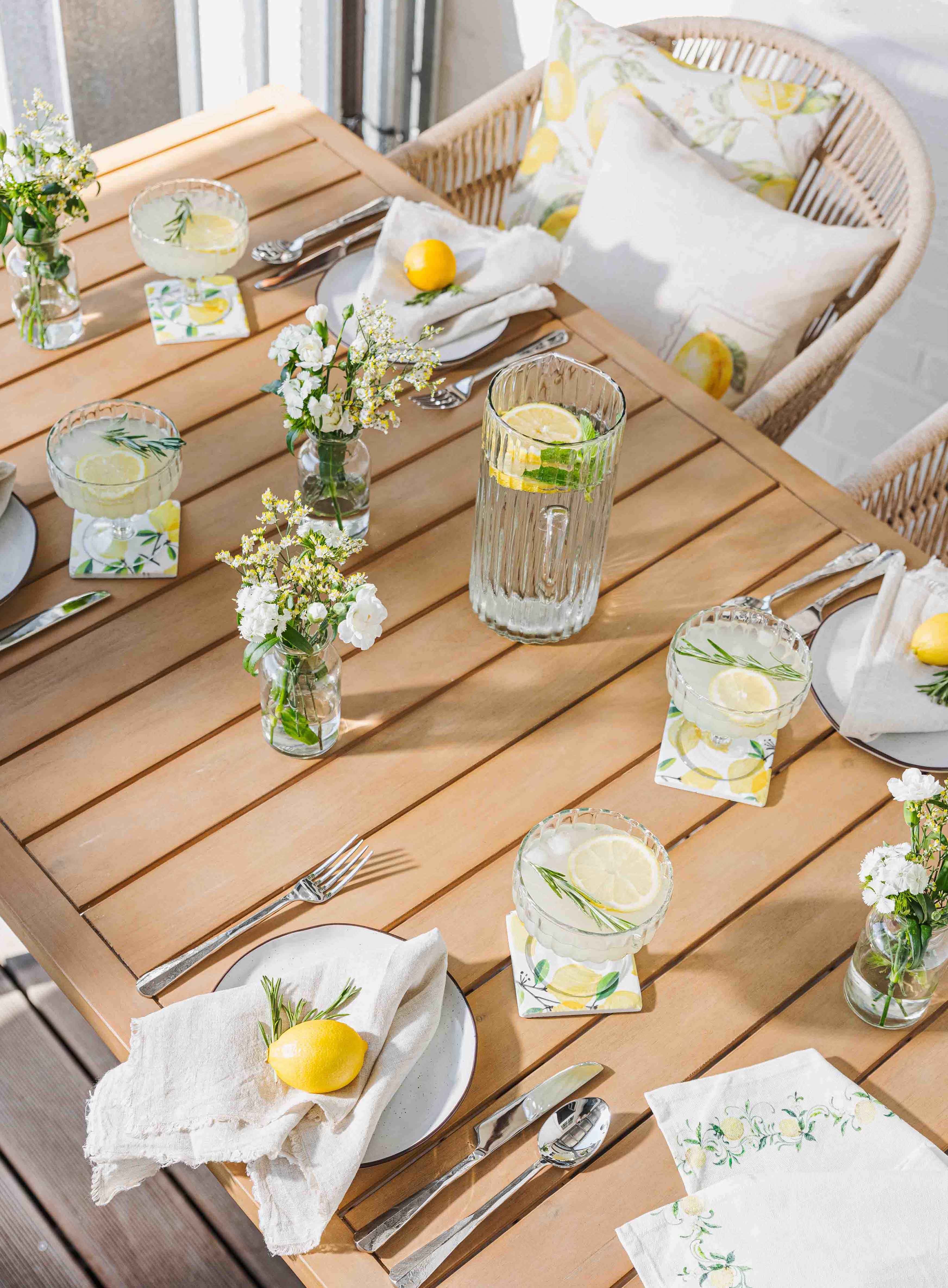 Tavolo in legno chiaro con limonata, bicchieri e decorazioni al limone per un'atmosfera estiva in giardino
