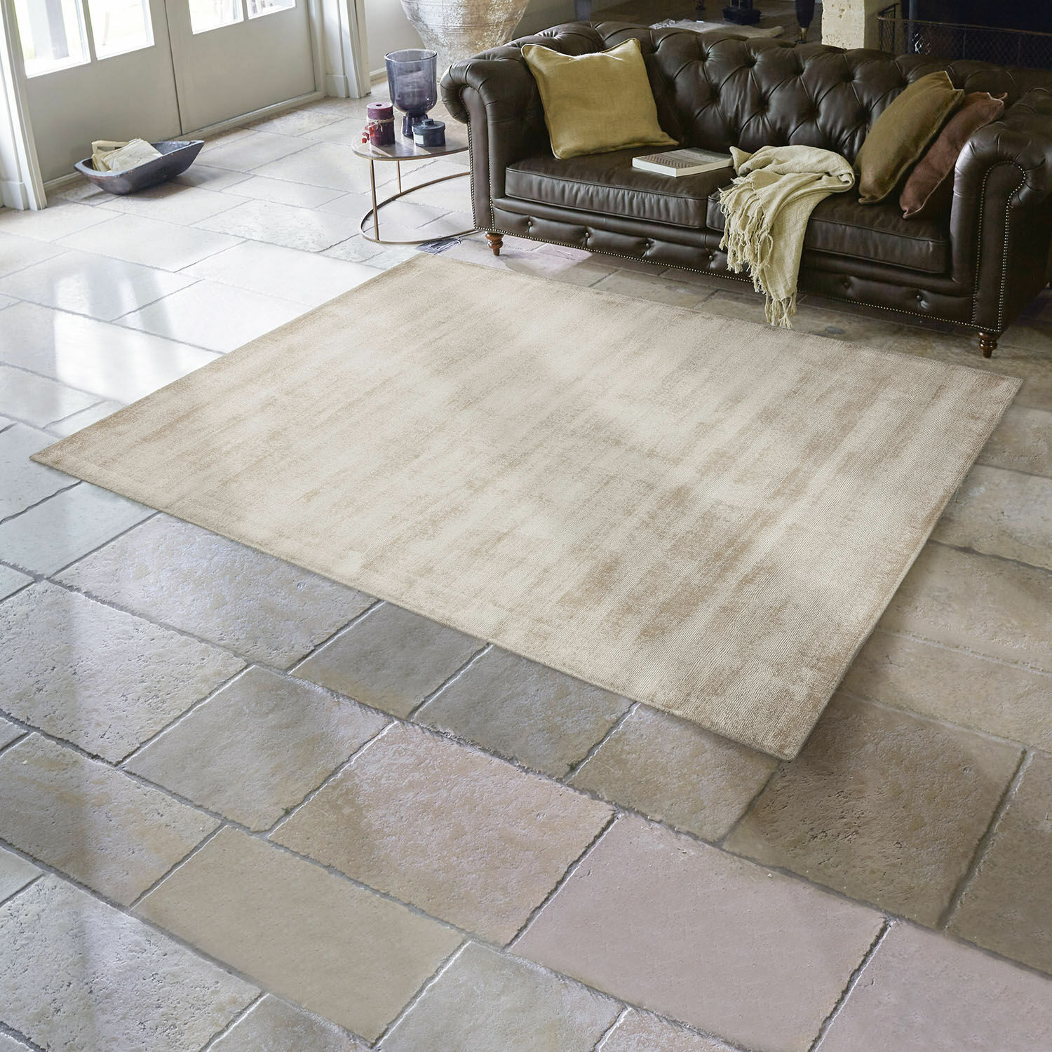 Tappeto Mariselle Tappeto beige in materiale morbido su pavimento in pietra con divano in pelle marrone scuro