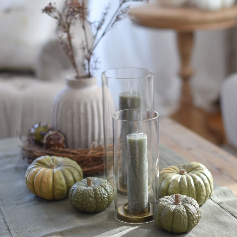 Candele verdi decorative e zucche in portacandele di vetro su tavolo in legno in stile naturale