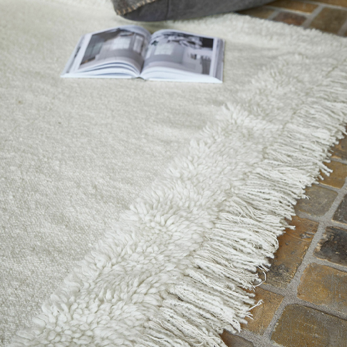 Tappeto bianco con bordo a frange morbide su pavimento in pietra, decorazione d'interni