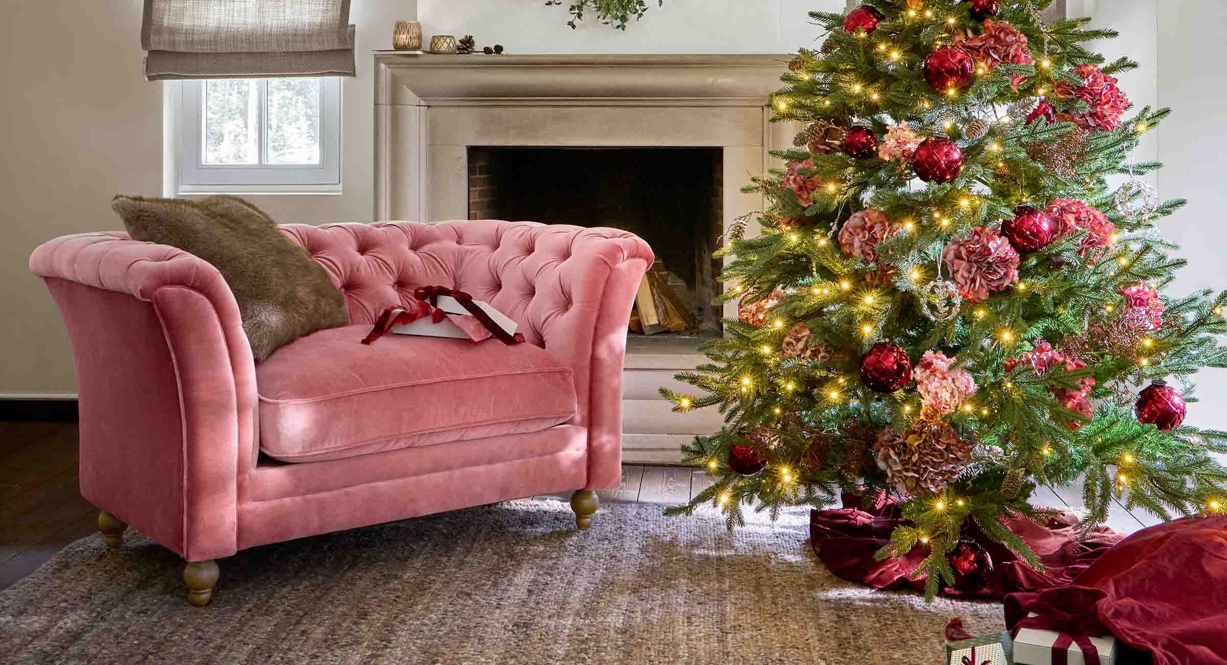 Divano in velluto rosa accanto a un albero di Natale decorato con palline rosse e luci festive