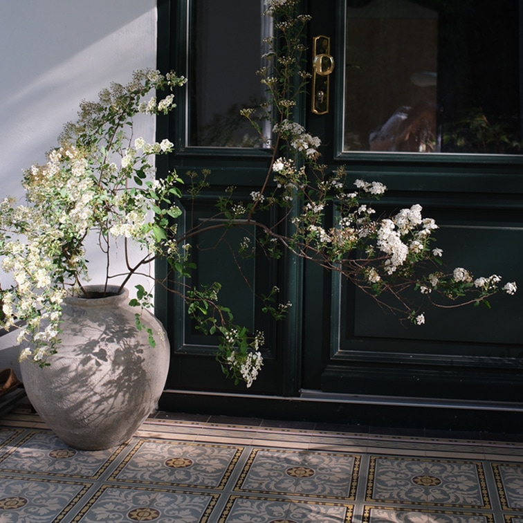 Grande vaso in ceramica con fiori bianchi davanti a porta scura e pavimento piastrellato decorativo