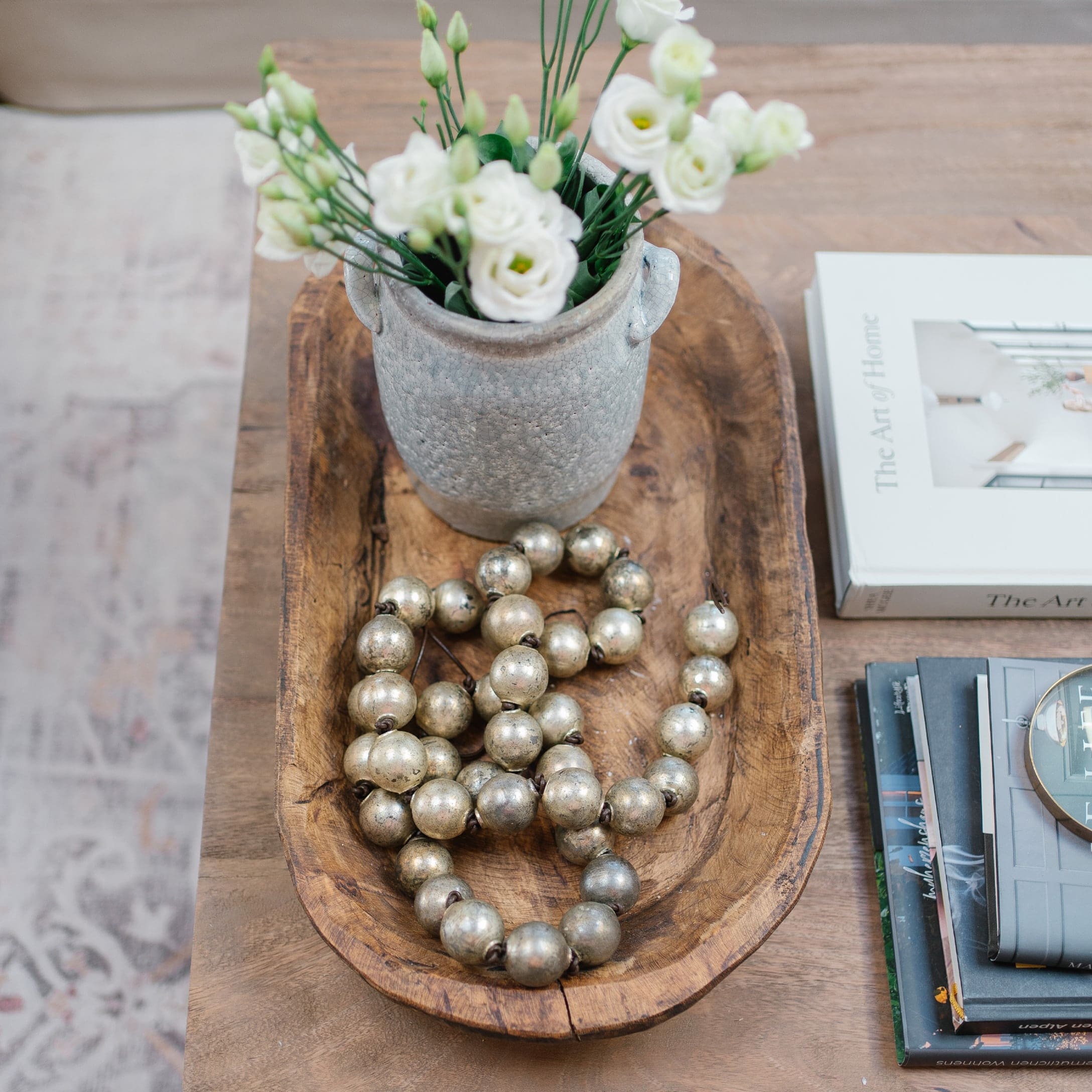Ciotola in legno con vaso in ceramica grigia, fiori bianchi e collana decorativa di perle metalliche