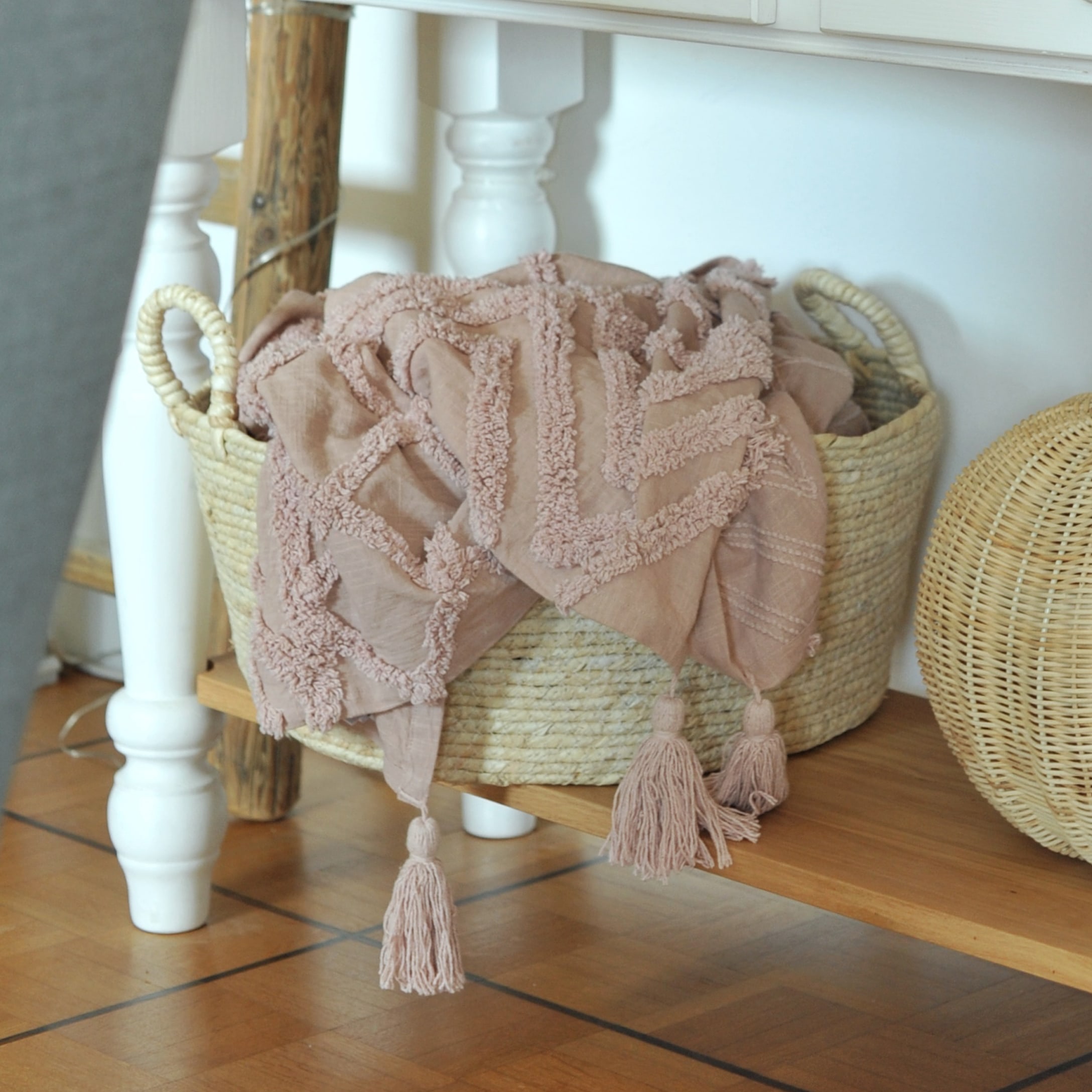 Coperta decorativa rosa con nappe in tessuto morbido in cesta di vimini su mensola in legno