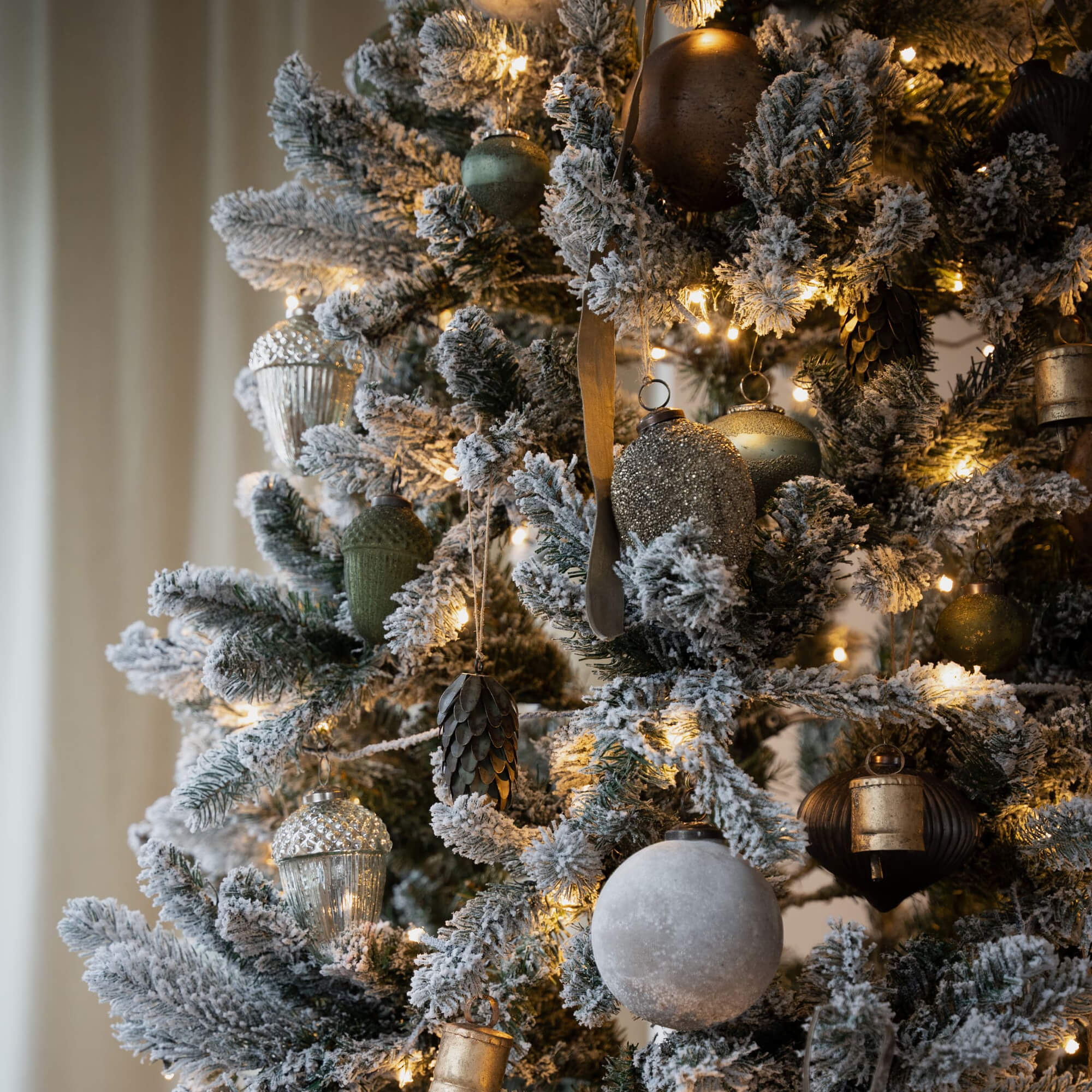 Albero di Natale artificiale con rami innevati e decorazioni dorate e verdi, luci natalizie