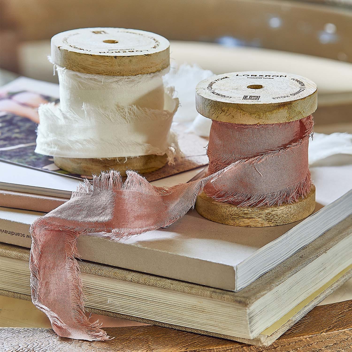Bobine di legno con tessuto sottile bianco e rosa su una pila di libri per decorazione d'interni