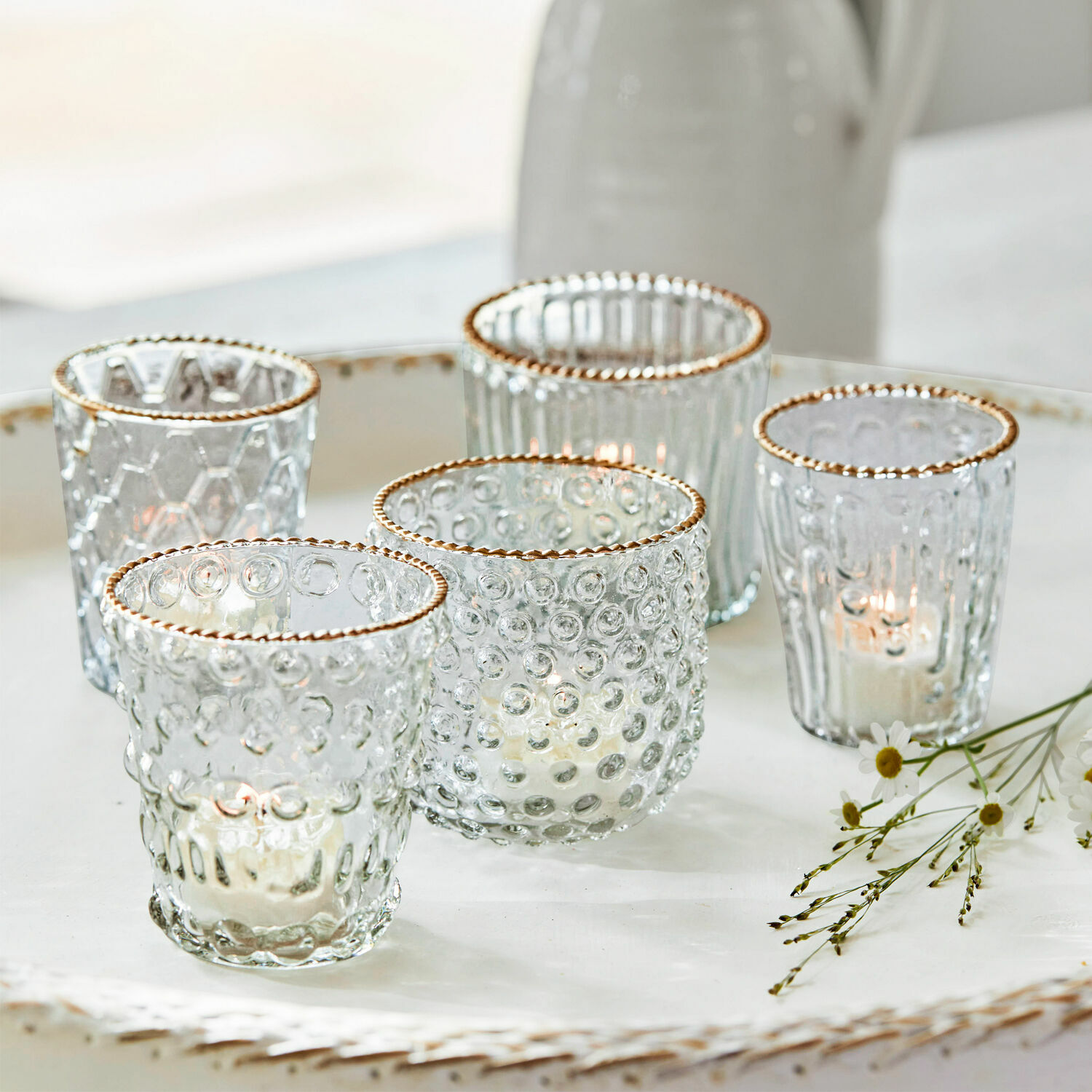 Set di 5 portalumini Jarnac Set di cinque portacandele in vetro con bordo dorato e texture, su vassoio bianco decorativo