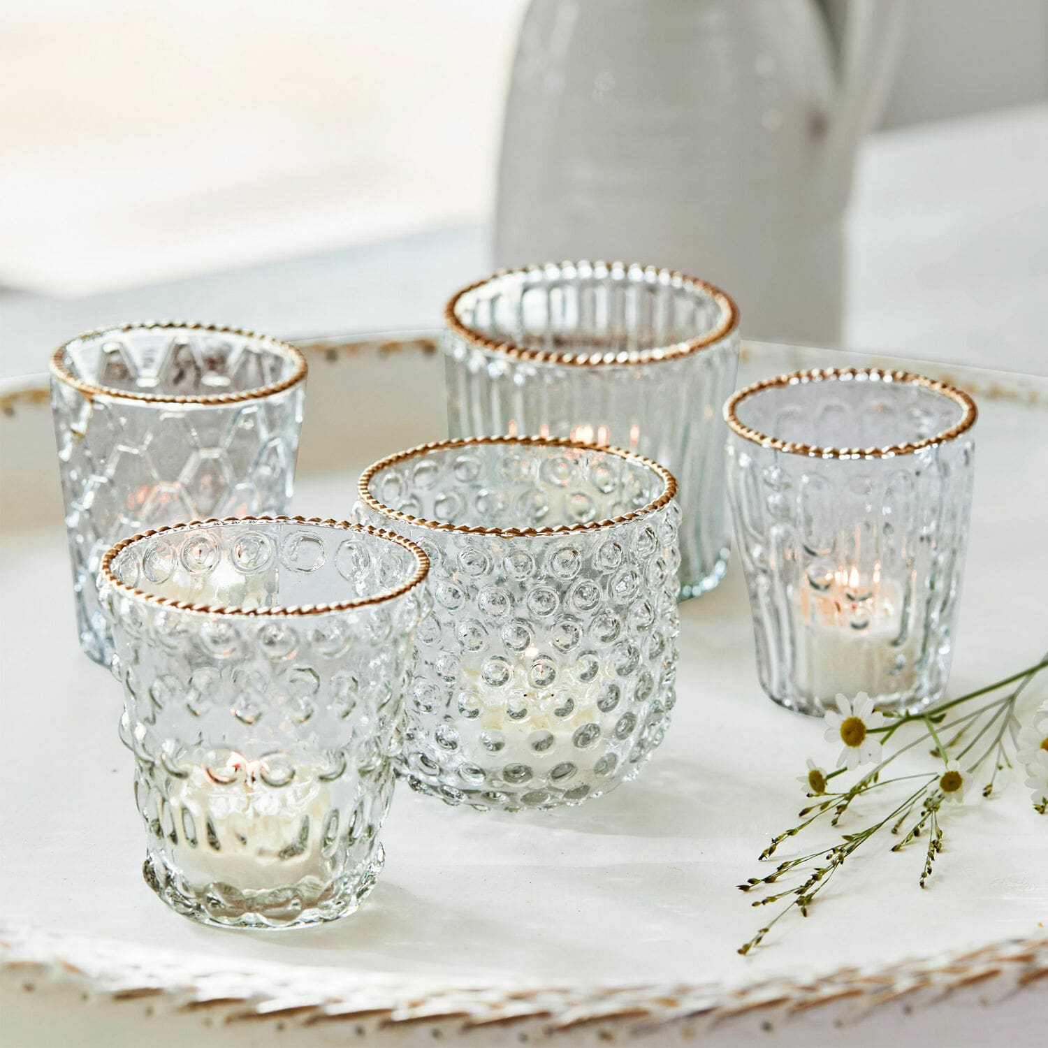 Set di 5 portalumini Jarnac Set di cinque portacandele in vetro con bordo dorato e texture, su vassoio bianco decorativo