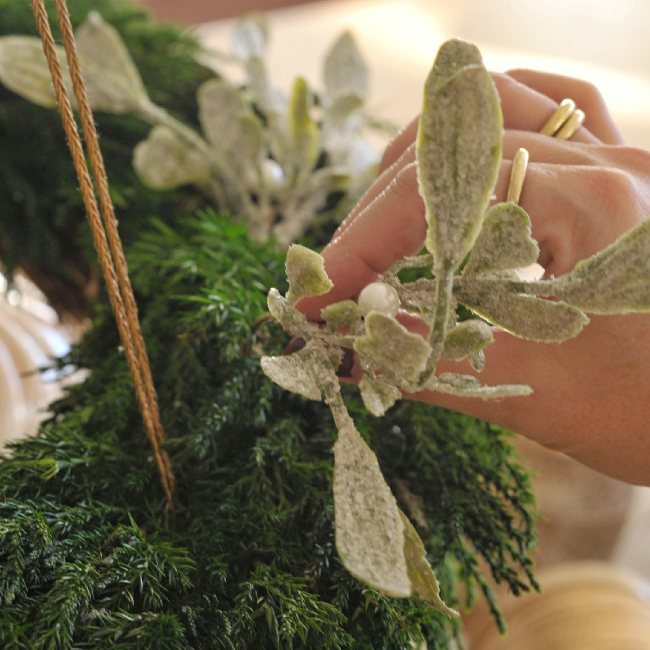 Mano che decora corona d'Avvento verde con foglie bianche e perle per decorazioni natalizie