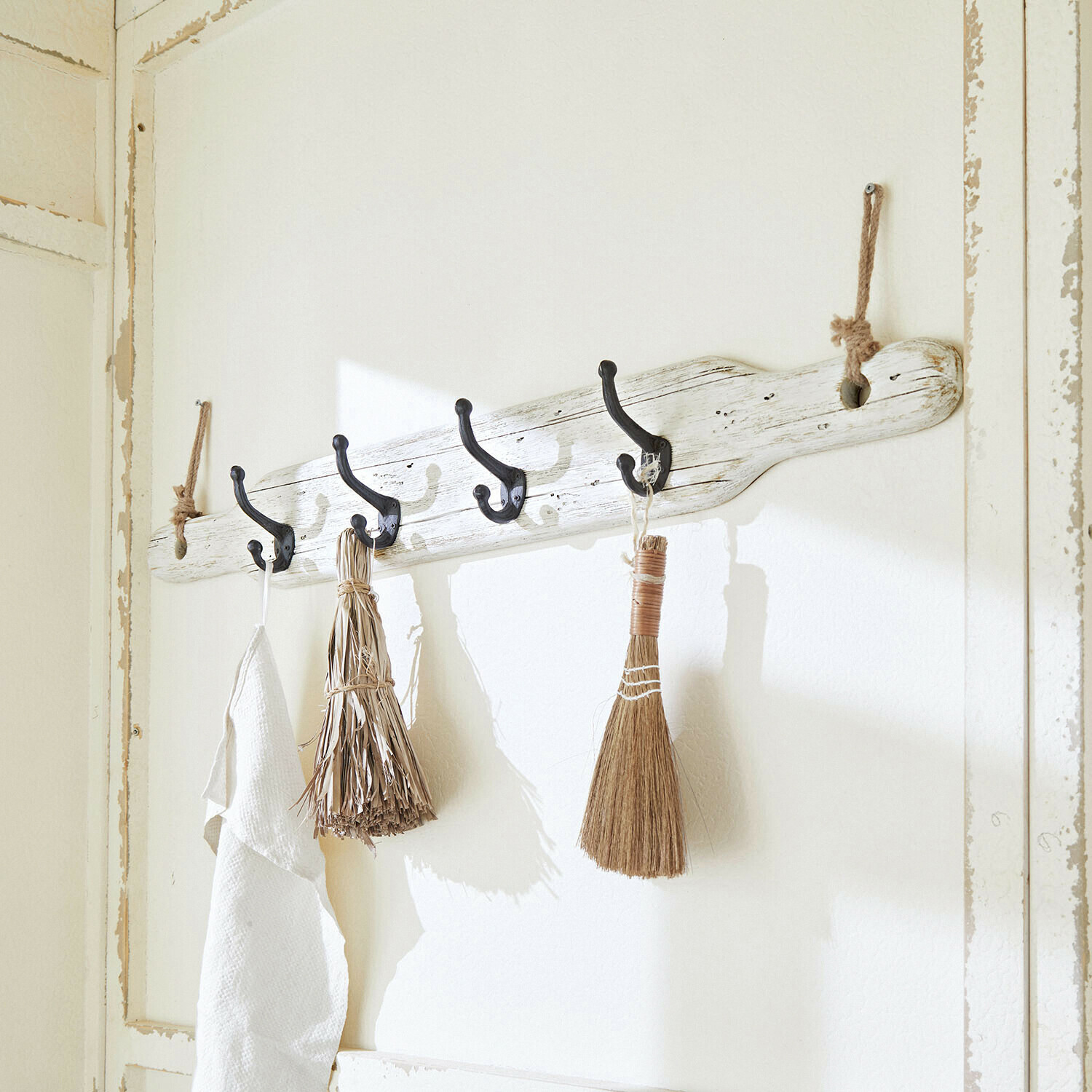 Appendiabiti da parete rustico in legno bianco con ganci neri e scope decorative naturali