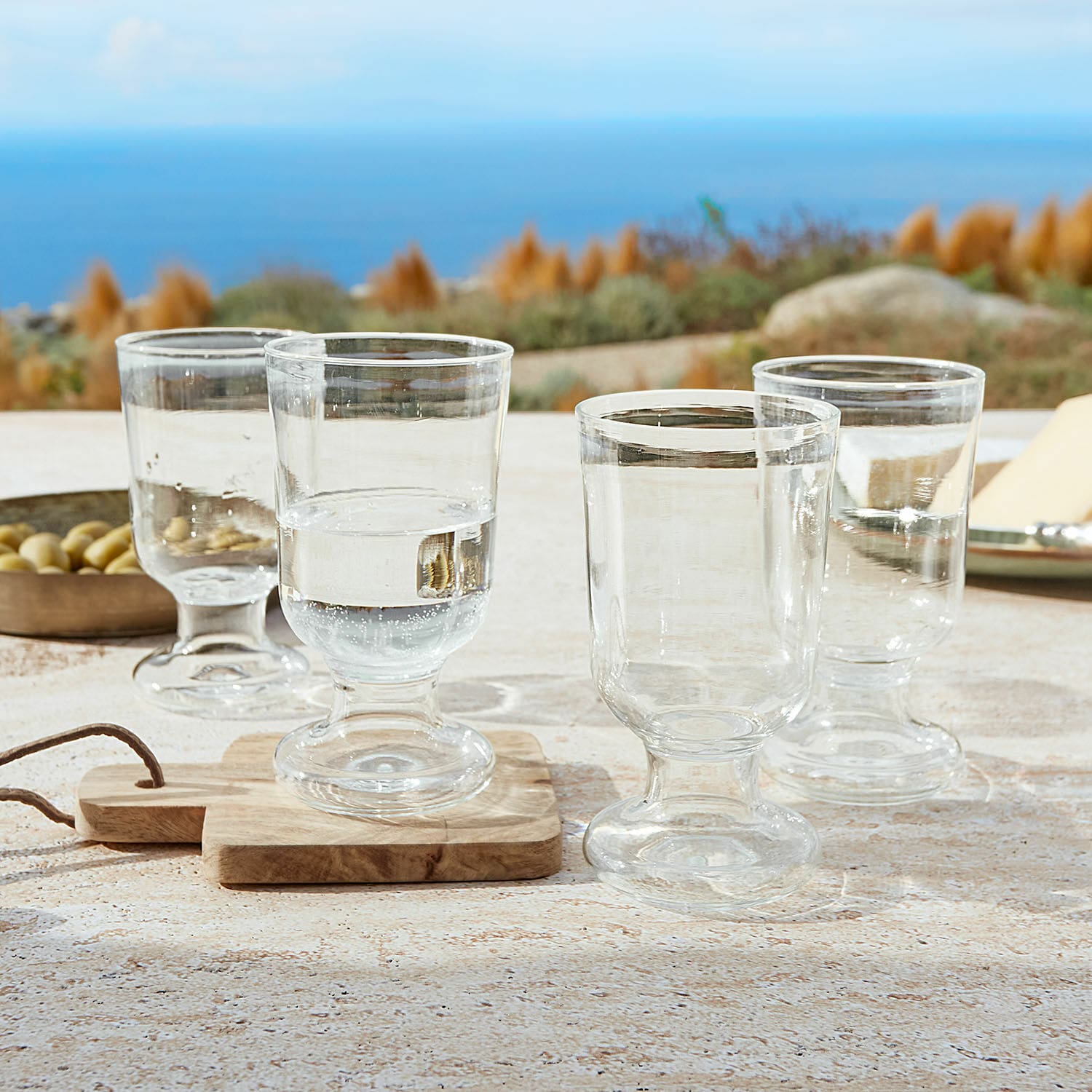 Set di 4 bicchieri Yvoncourt Set di quattro bicchieri trasparenti con base su tavolo con vista mare
