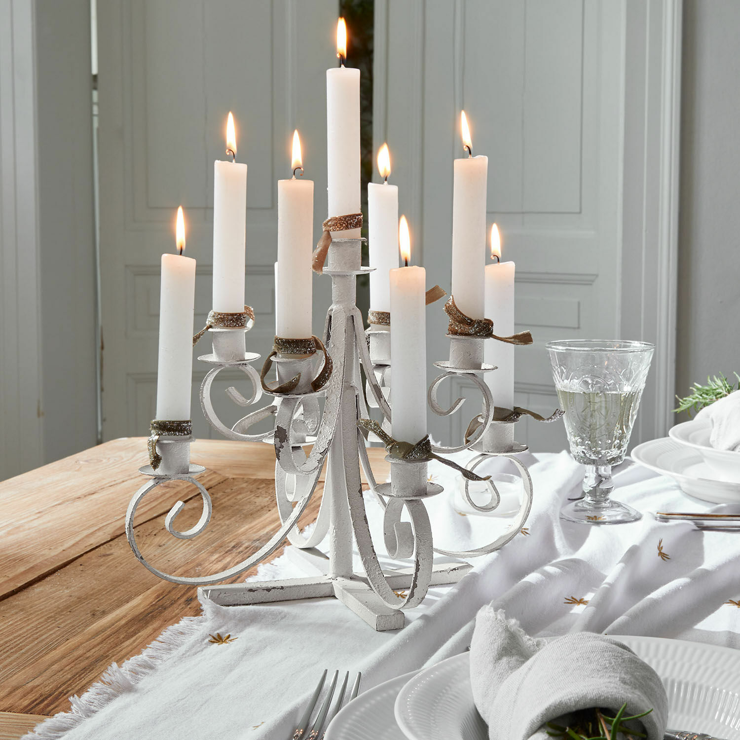 Portacandele Siolagh Candelabro bianco in metallo con nove candele accese su tavolo in legno decorato per cena