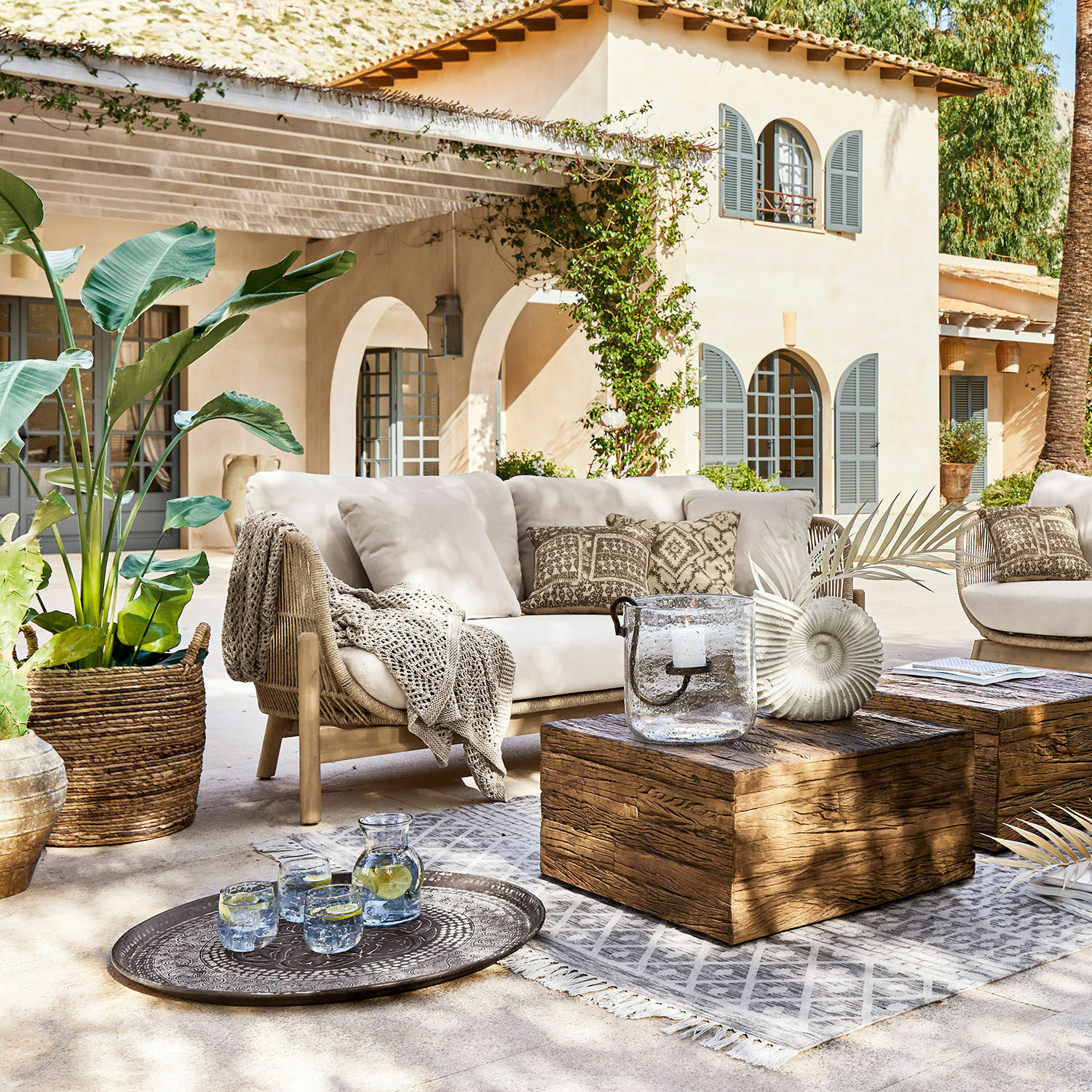 Divano FSC®-100% Belvidere Set di mobili da esterno con divano beige, tavolo in legno e decorazioni su terrazza soleggiata
