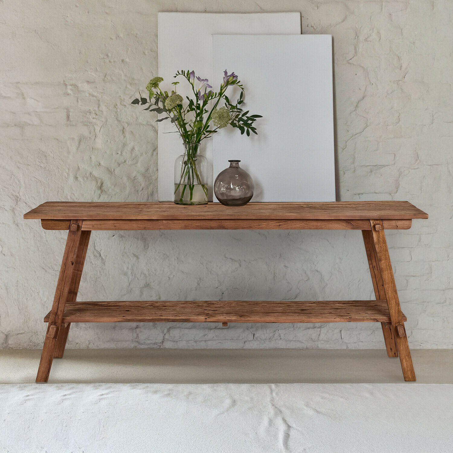 Consolle Brévonne Tavolo in legno naturale con ripiano, decorato con vasi e fiori davanti a muro bianco