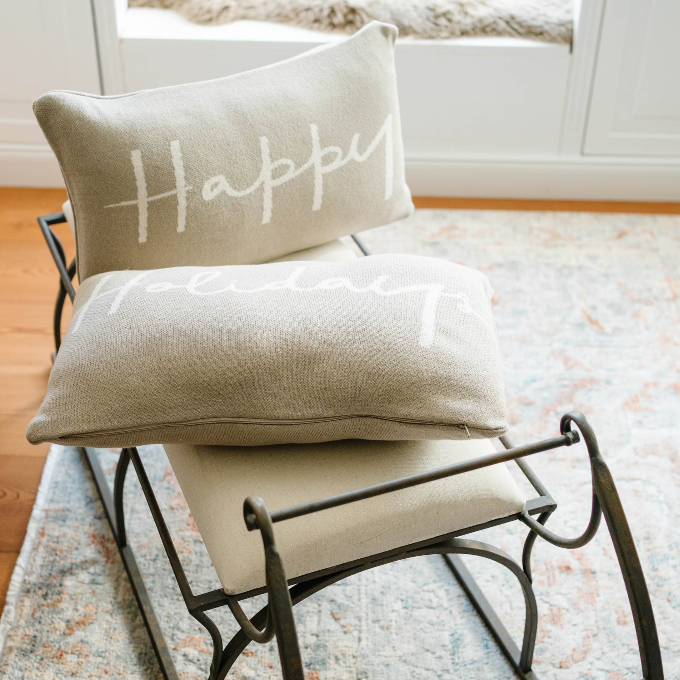 Cuscini beige con scritta Happy Holidays su struttura metallica su tappeto chiaro