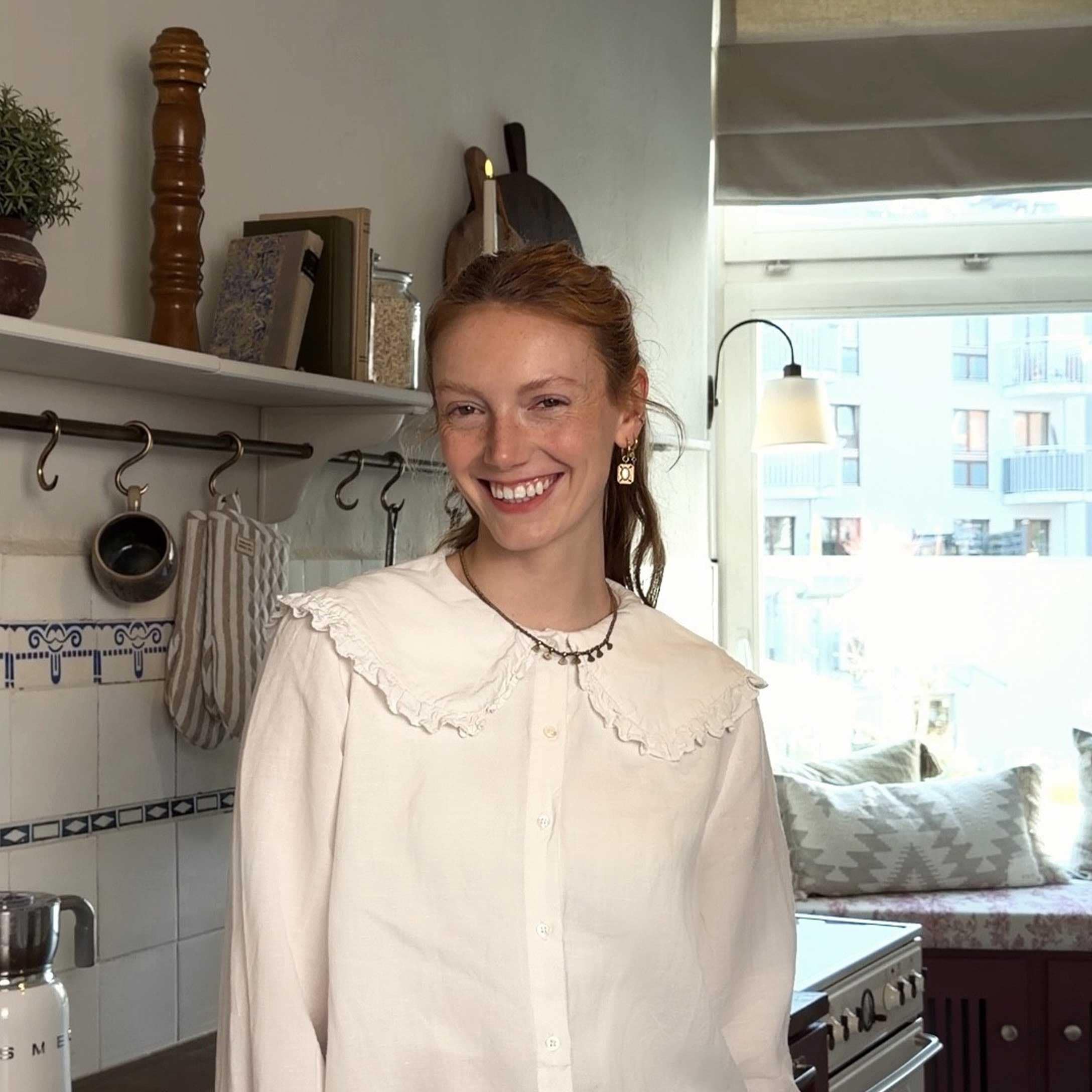 Donna con camicetta bianca con volant in cucina luminosa con accessori decorativi e finestra