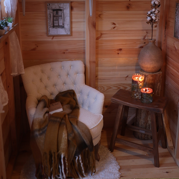 Angolo accogliente con poltrona bianca trapuntata, coperta marrone e sgabello in legno con candele accese