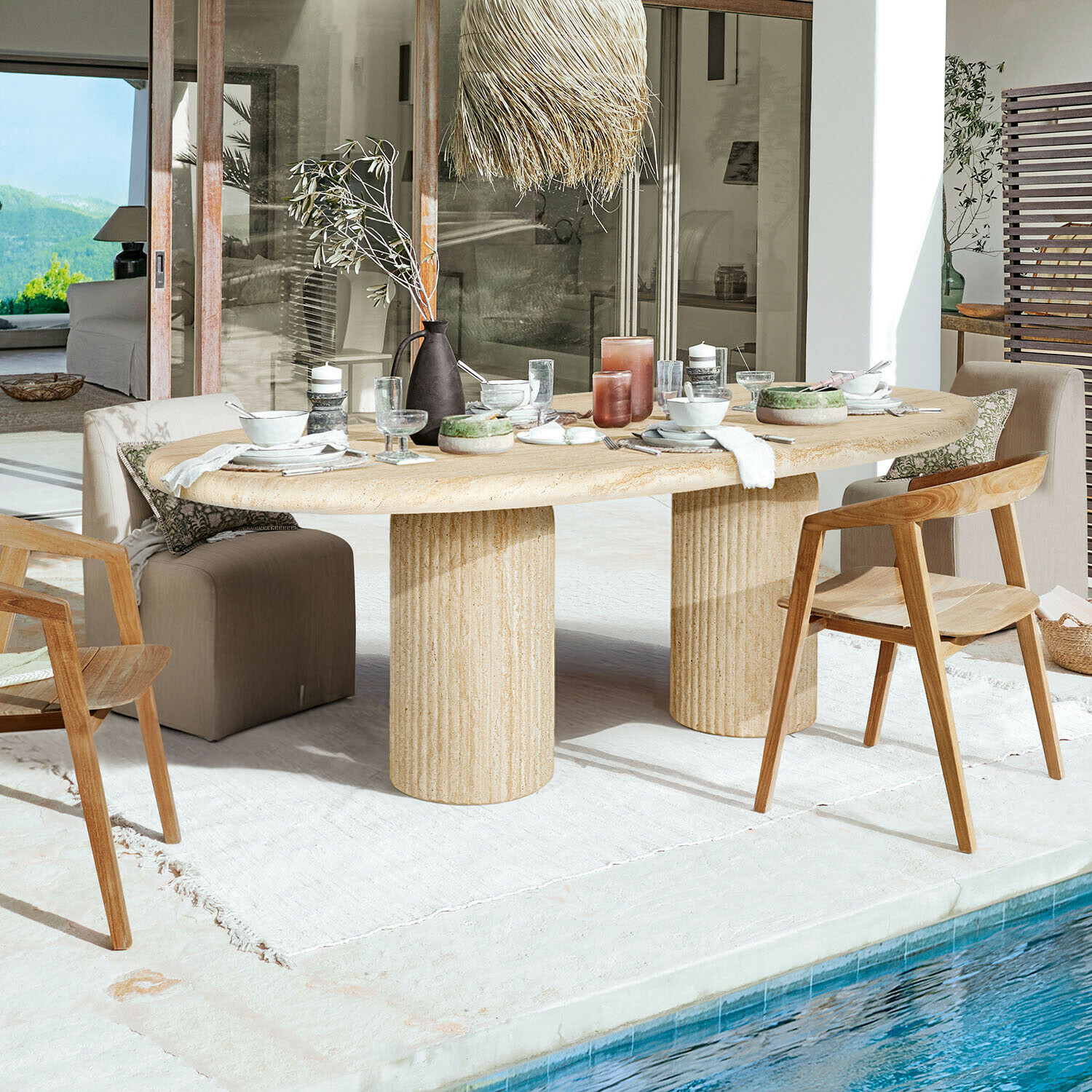 Tavolo Calerio Tavolo ovale in pietra beige con due gambe cilindriche su terrazza vicino piscina con sedie in legno