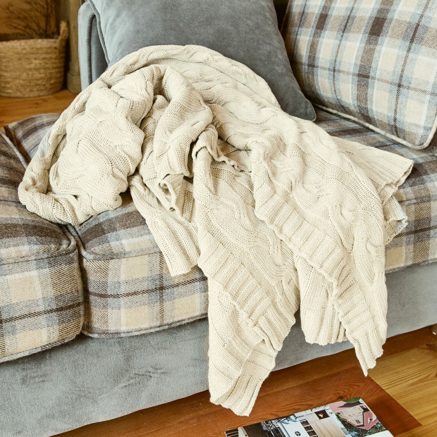 Coperta Arnhem Coperta beige in cotone lavorata a maglia su divano grigio a quadri beige in soggiorno