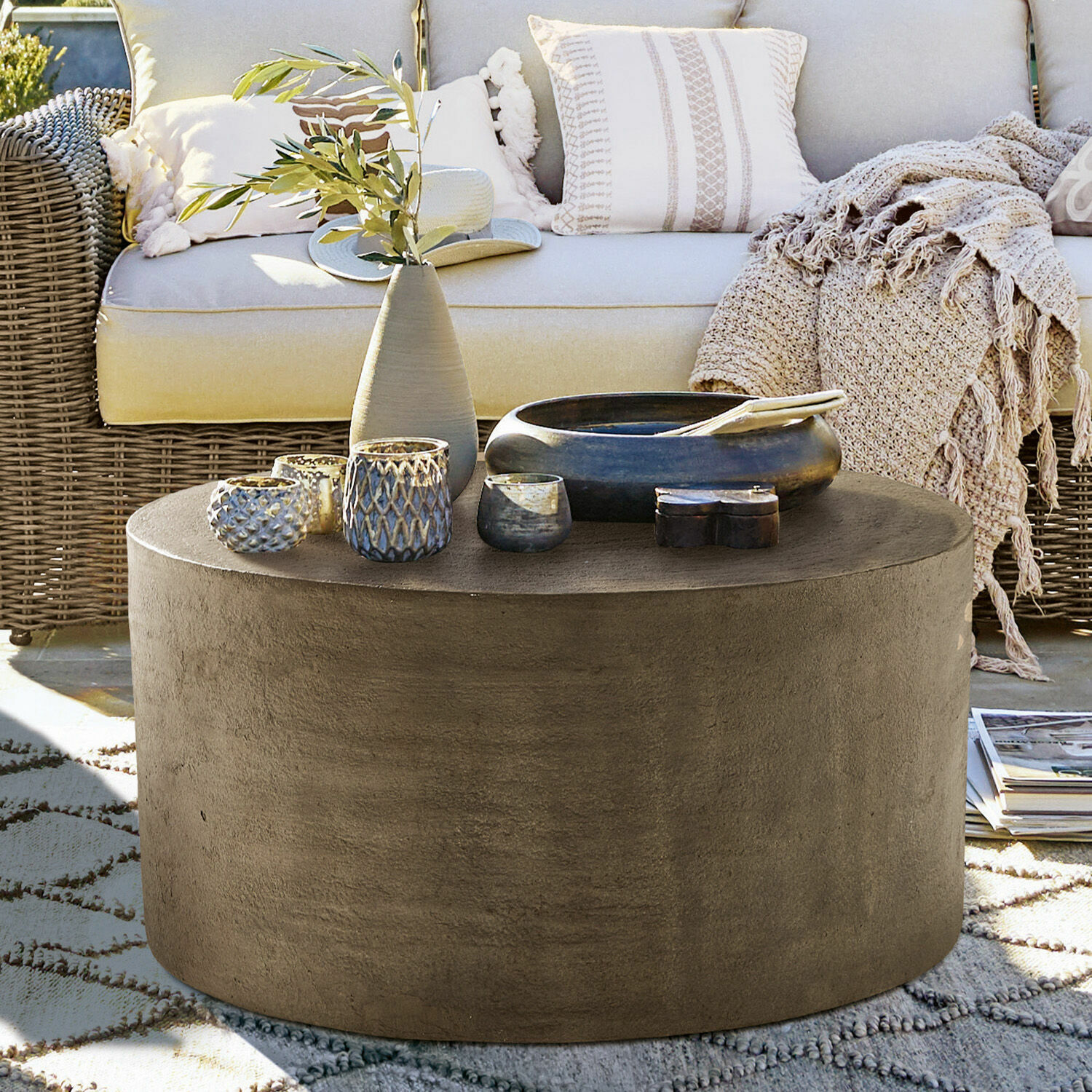 Tavolino da salotto Lexy Tavolino rotondo in cemento grigio su terrazza con decorazioni e divano in rattan