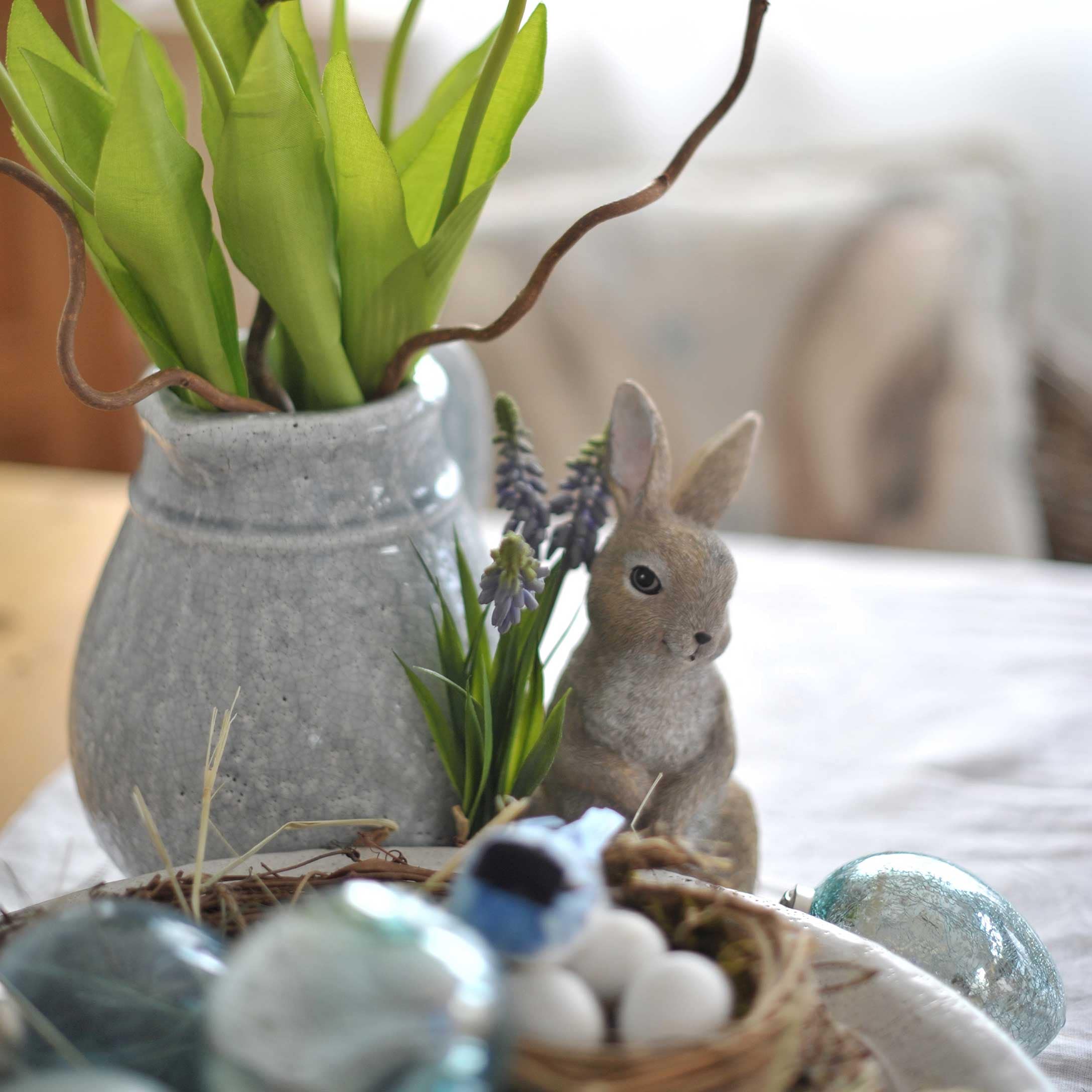 Vaso in ceramica grigia con foglie verdi e figura di coniglio come decorazione pasquale sul tavolo