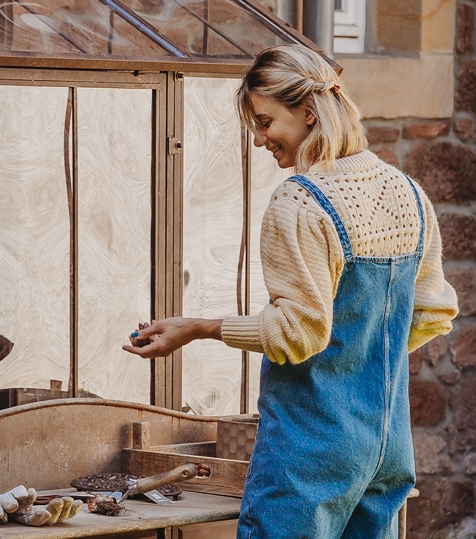 Donna con salopette blu e maglione crema che lavora a un tavolo di legno in giardino