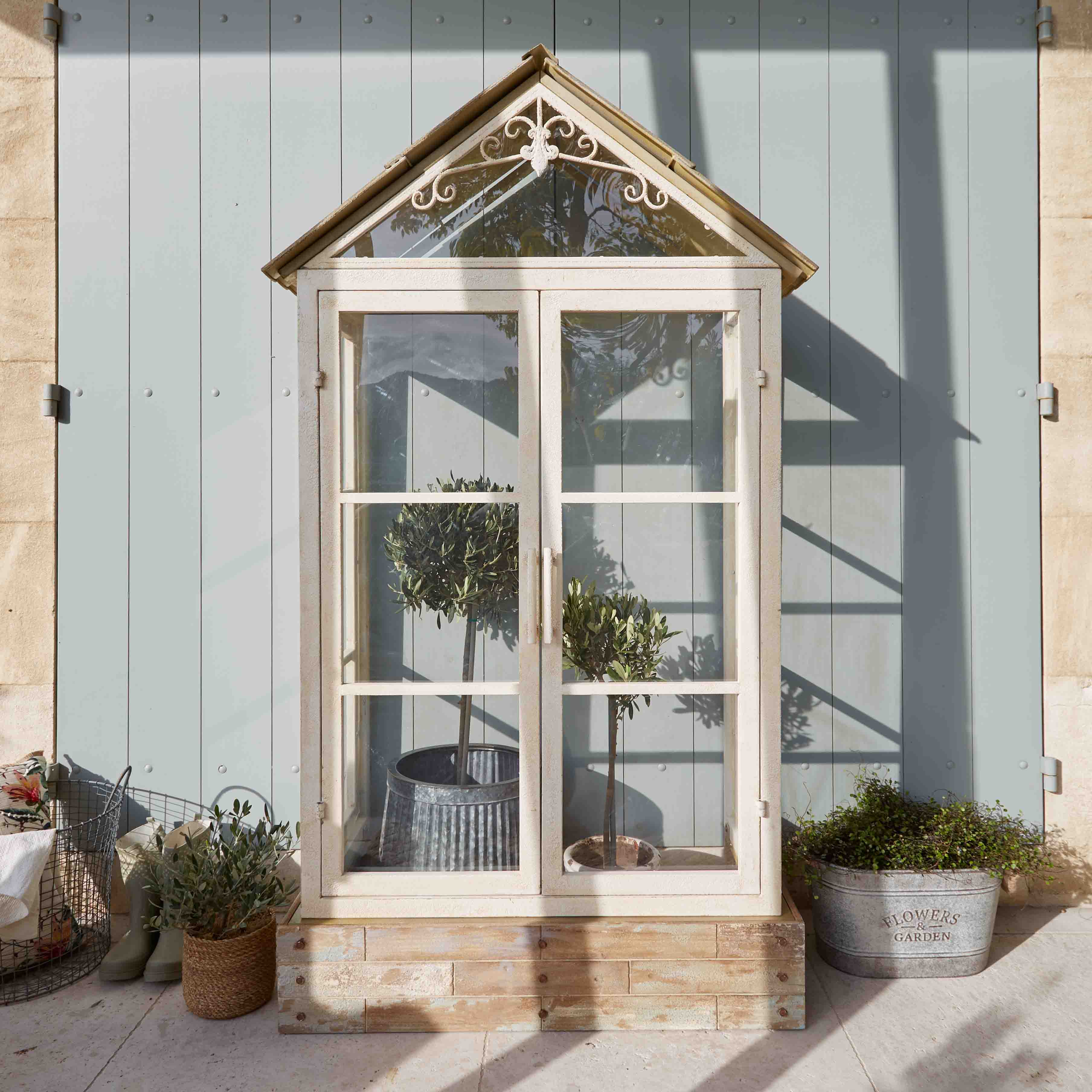 Serra bianca in legno con tetto decorativo e piante in vaso su terrazza soleggiata