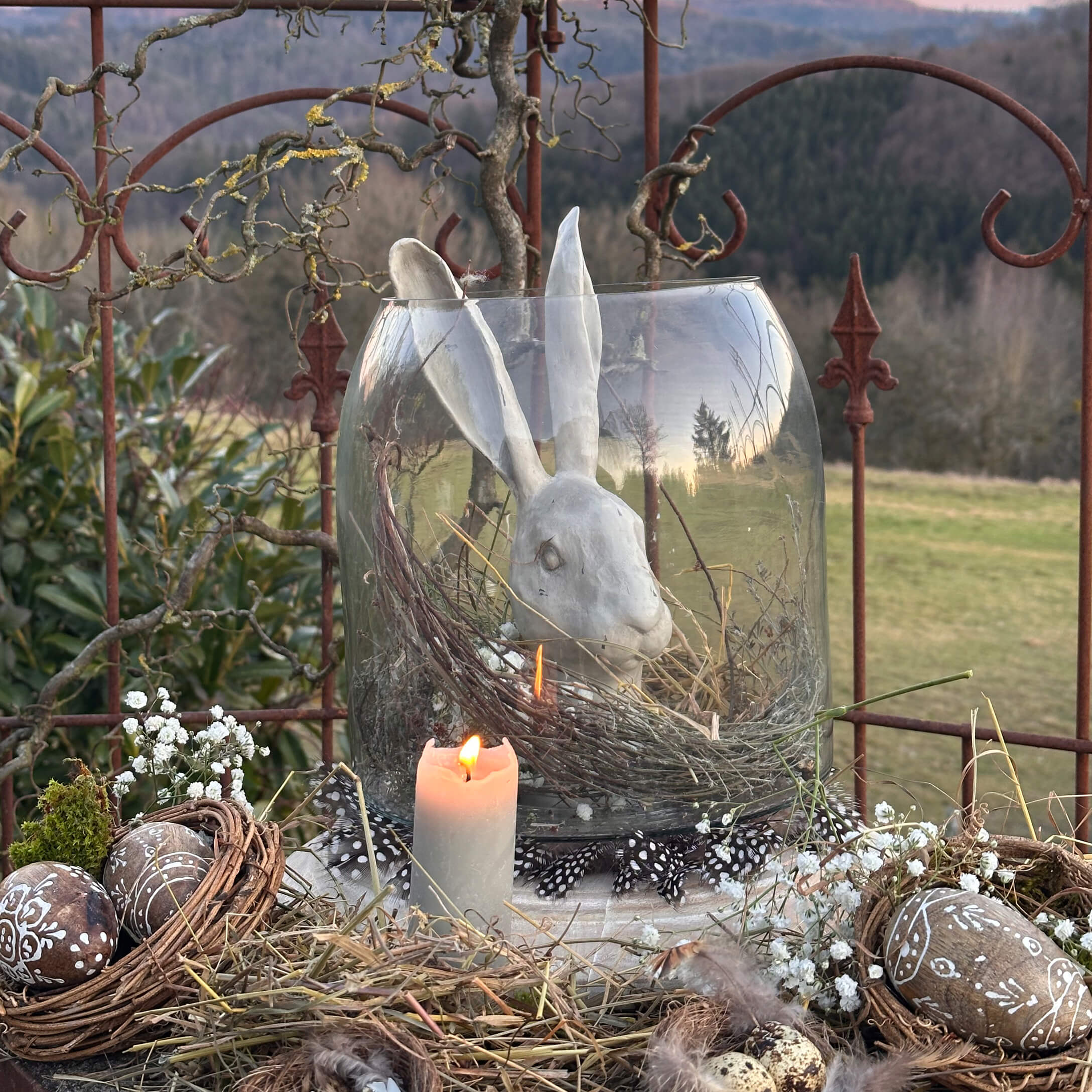 Decorazione pasquale con coniglio in ceramica bianca in vaso di vetro e candela accesa rustica