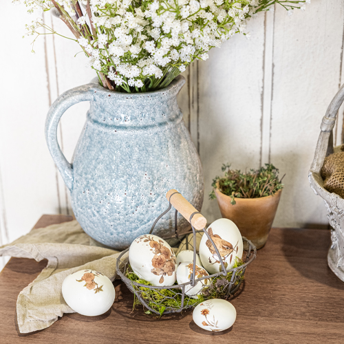 Brocca in ceramica blu con fiori bianchi e uova decorative con motivi animali su tavolo in legno